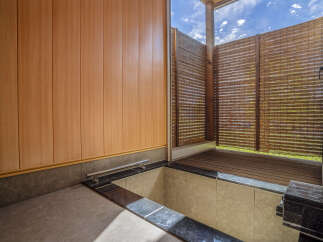Experience tranquility in this outdoor bathing area, featuring a deep soaking tub with a sleek chrome handle and elegant dark stone accents.