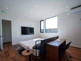 This modern studio apartment features a comfortable bed, a functional workspace with a desk and chair, and a large window offering ample natural light.