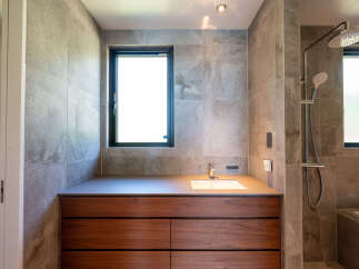 Experience modern luxury in this stunning bathroom, featuring a sleek vanity with rich wood cabinetry and a pristine white sink.
