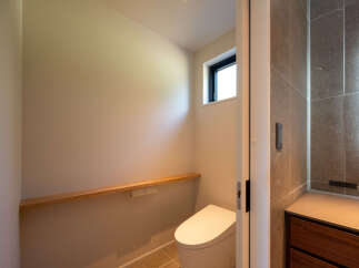 Discover modern comfort in this well-appointed bathroom, featuring a sleek, contemporary toilet and a minimalist wooden shelf for added storage and style.