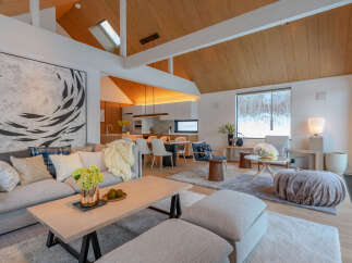 Experience luxurious mountain living in this stunning open-concept living space, featuring a vaulted wood-paneled ceiling and a large abstract artwork.