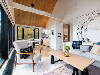 Experience modern living in this stunning open-concept space, featuring a sleek kitchen with light wood cabinetry and a bright dining area overlooking a scenic autumn landscape.