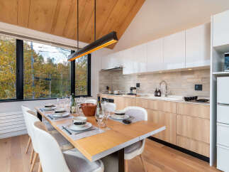 Experience modern living in this stunning dining area and kitchen, featuring a sleek linear pendant light and a large window with picturesque forest views.