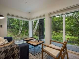 Experience seamless indoor-outdoor living in this modern retreat, featuring expansive floor-to-ceiling windows that flood the space with natural light and offer breathtaking views of the surrounding lush greenery.