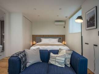 Discover modern comfort in this stylish studio apartment, featuring a cozy bed area with bedside lamps and a plush blue sofa perfect for relaxation.