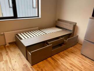 Discover modern comfort in this bedroom featuring a stylish wooden bed frame with integrated storage drawers, perfect for maximizing space.