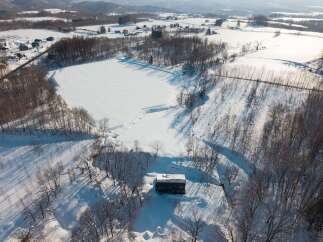Discover this secluded winter retreat, a charming house nestled amidst snow-covered landscapes and bare trees.