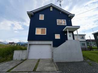 Discover this modern dark blue home featuring a convenient roll-up garage door on the lower level and a welcoming entrance with a covered porch.