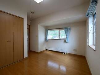 Discover this charming room featuring a spacious wooden wardrobe and a large window with light blue curtains, offering a view of the outdoors.
