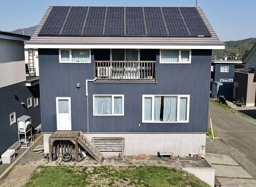 Discover this modern two-story home featuring a sleek, dark blue corrugated metal exterior and a prominent balcony on the second floor.