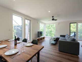 Experience modern living in this spacious open-concept dining and living area, featuring a large wooden dining table set for a meal and a comfortable grey sectional sofa.