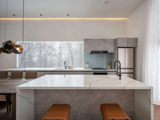 Experience modern luxury in this stunning kitchen featuring a sleek island with a waterfall countertop and integrated seating.