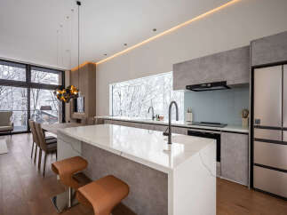 Experience modern luxury in this stunning kitchen and dining area, featuring a sleek island with a waterfall countertop and comfortable bar stools.