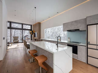 Experience modern luxury in this stunning open-concept kitchen and living area, featuring a sleek white island with a waterfall edge and comfortable leather bar stools.
