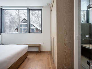 Experience serene winter living in this modern bedroom featuring a large window with picturesque snow-covered views.