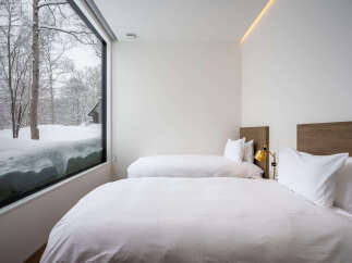 Experience cozy winter nights in this modern bedroom featuring two comfortable beds and a large window overlooking a snowy landscape.