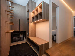 Discover modern elegance in this entryway, featuring a sleek wooden bench with integrated shoe storage and a stylish shelving unit illuminated by warm LED lighting.