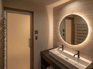 Experience modern luxury in this stunning bathroom featuring a sleek double vanity with contemporary black faucets and a backlit circular mirror.