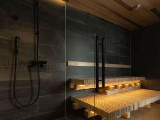 Experience ultimate relaxation in this modern spa sanctuary, featuring a sleek shower area with dark stone tiles and a luxurious wooden sauna bench illuminated by warm ambient lighting.