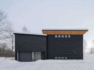 This modern home features a striking dark exterior with a contrasting wooden soffit under a snow-dusted roof.