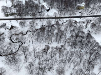 Experience serene winter living in this picturesque property nestled amidst snow-covered trees and a winding stream.