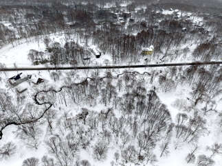 Discover a serene winter wonderland with this aerial view of a snow-covered landscape dotted with charming houses nestled amongst bare trees.