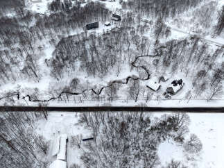 Experience serene winter living in this picturesque landscape, featuring a charming home nestled amidst snow-covered trees and a winding creek.