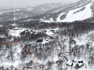 Discover this expansive winter wonderland, featuring a ski resort nestled amidst snow-covered mountains and dense forests.