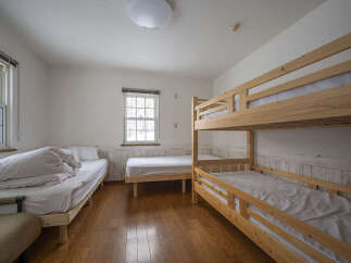 This spacious room features multiple sleeping arrangements, including a comfortable single bed with ample bedding and a sturdy wooden bunk bed.