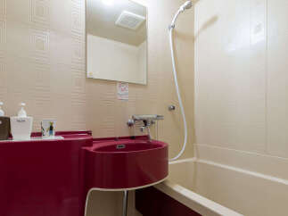 Discover this compact bathroom featuring a vibrant red sink and a clean, cream-colored bathtub.