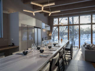 Experience modern luxury in this stunning open-concept living space, featuring a sleek kitchen island with ample seating and a breathtaking view of a snow-covered landscape through expansive windows.