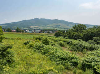 Discover serene living in this picturesque rural landscape, featuring a charming village nestled against rolling green hills and a majestic mountain backdrop.