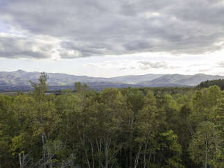 Experience breathtaking panoramic views from this property, showcasing rolling hills and majestic mountains under a dramatic sky.