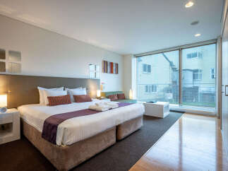 Experience modern comfort in this spacious studio apartment, featuring a plush king-sized bed and a cozy seating area perfect for relaxation.