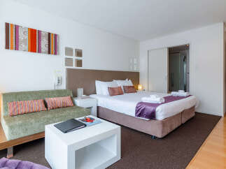 Experience comfort and style in this modern hotel room, featuring a plush king-sized bed with luxurious purple accents and a cozy green sofa perfect for relaxation.