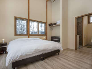 Experience serene living in this spacious bedroom featuring a large bed, ample natural light from the windows, and a convenient open closet space.