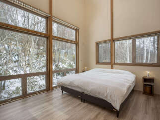 Experience serene winter living in this charming bedroom, featuring expansive floor-to-ceiling windows that offer breathtaking views of a snow-covered forest.