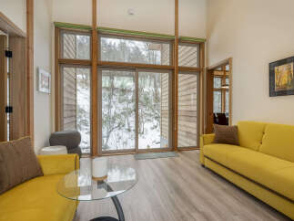 Experience modern living in this bright and airy living room, featuring a stunning wall of windows that floods the space with natural light and offers picturesque views of the surrounding winter landscape.