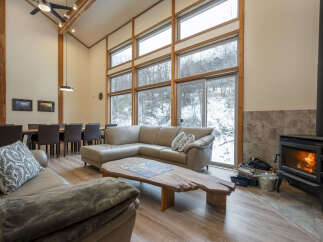 Experience cozy living in this spacious great room, featuring a soaring vaulted ceiling with exposed beams and a stunning wall of windows overlooking a winter wonderland.