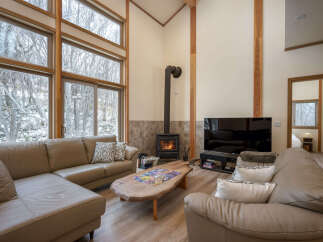 Experience cozy living in this stunning mountain retreat, featuring a spacious sectional sofa perfect for gathering around the wood-burning fireplace.