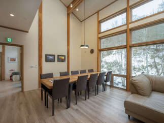 Experience luxury living in this spacious dining area, featuring a large wooden table perfect for gatherings and floor-to-ceiling windows offering breathtaking winter forest views.