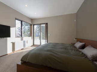 Experience serene winter views from this cozy bedroom, featuring a large window and sliding glass doors that open to a snowy landscape.