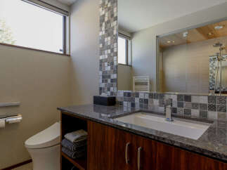 This modern bathroom features a sleek vanity with a granite countertop, a minimalist toilet, and a spacious walk-in shower visible in the reflection.