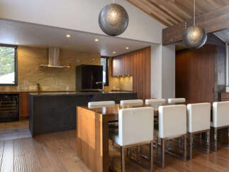 Experience modern luxury in this stunning kitchen and dining area, featuring sleek wood cabinetry and a dramatic stone island.