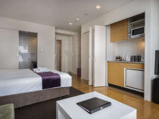 This modern studio apartment offers a comfortable queen-sized bed with luxurious purple accents and a convenient kitchenette equipped with a microwave and mini-fridge.