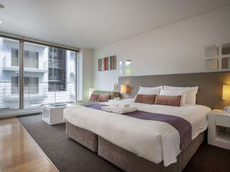 Experience modern comfort in this stylish hotel room, featuring a plush king-sized bed adorned with elegant purple accents and decorative pillows.