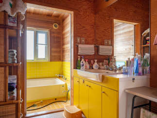 This charming bathroom features a bright yellow tiled shower and bathtub area, complemented by warm wooden walls and cabinetry.