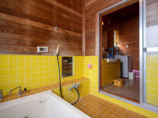 Experience a unique bathroom design featuring vibrant yellow tiled walls and floors, complemented by warm wooden paneling on the ceiling and upper walls.