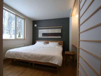 Experience serene living in this minimalist bedroom, featuring a spacious king-size bed with crisp white linens and a striking abstract artwork above the headboard.