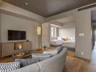 Experience modern comfort in this spacious hotel suite, featuring a stylish living area with a large TV and a sleek entertainment console.